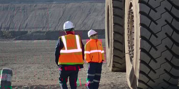 Two workers in hard hats and safety vests standing near the massive tire