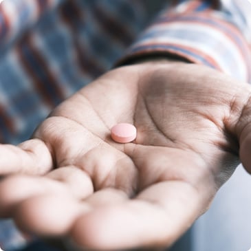 A hand holding a single pink pill