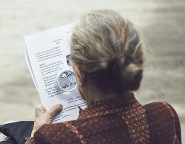 older woman reading a document using a magnifying glass